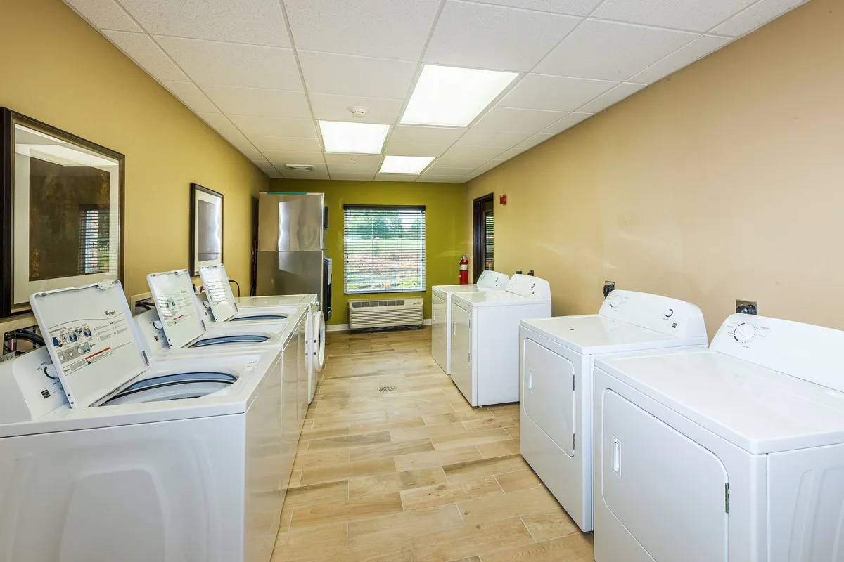 A bright and practical laundry room outfitted with washing machines, dryers, and a large window bringing in natural light. The area feels welcoming and functional, catering to guests' extended stay needs.