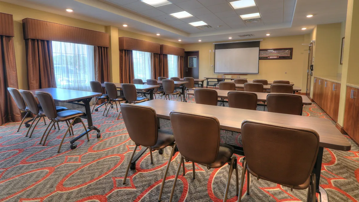 A well-organized business center interior featuring tables, chairs, and a large presentation screen. The space is designed for meetings, workshops, and presentations, with a focused and productive atmosphere that supports business activities.