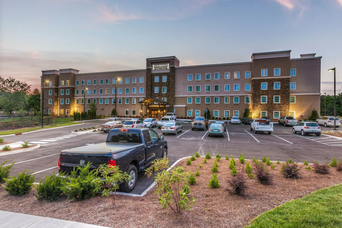 A welcoming hotel entrance set amid landscaped greenery, with guests arriving and gathering. The parking lot hints at easy access to nearby attractions, and the overall environment is vibrant and inviting, suggesting a gateway to local experiences.