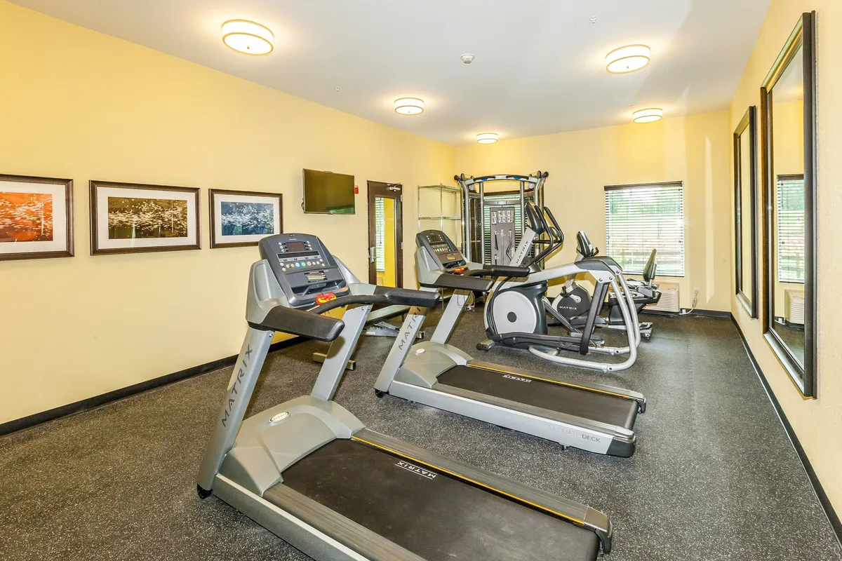A modern fitness facility filled with treadmills, an elliptical machine, mirrors, and other exercise equipment. The room is inviting and energizing, encouraging guests to maintain their fitness routines during their stay.