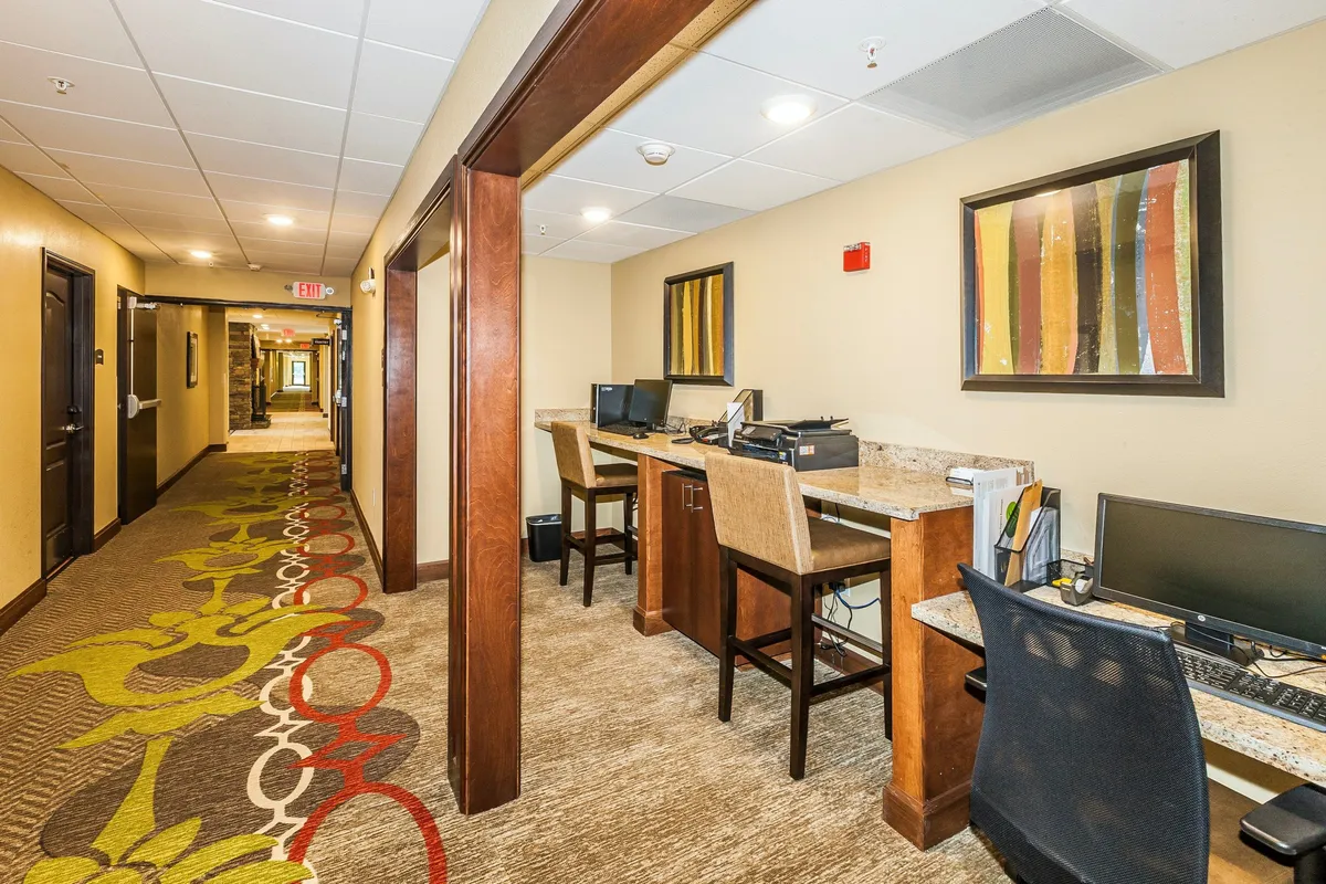 The photo presents a well-lit corner of the studio or communal interior, featuring computer workstations, modern decorative art, and a patterned carpet. The atmosphere is calm and conducive to productivity, ideal for guests needing a dedicated work area within or near their suite.