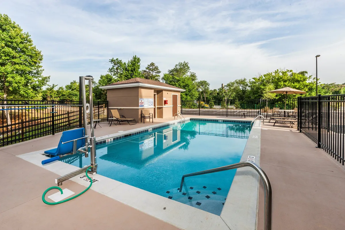 A bright, sunlit view of the hotel's outdoor swimming pool surrounded by inviting poolside lounge chairs and a shaded structure. The vibrant blue water glistens under clear skies, with ample space for guests to relax, sunbathe, or gather for casual poolside fun. The atmosphere is lively yet comfortable, ideal for both families and groups of friends.